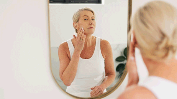 Woman applying lotion to face in mirror